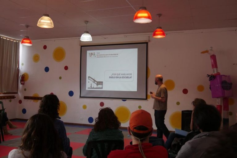 Aula con jóvenes mirando a Alejandro Nespral, quien expone utilizando una diapositiva con el título: ¿Por qué hablar de duelo en la escuela?