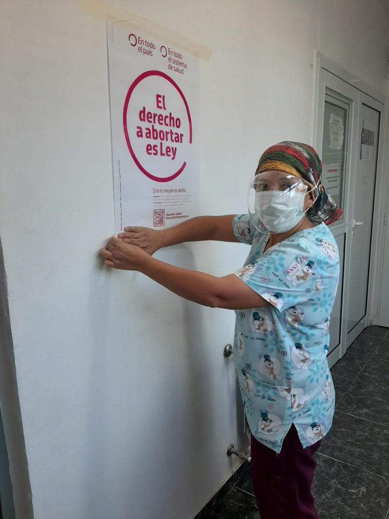 Personal de salud pegando un cartel en una sala de hospital con la leyenda "El derecho a abortar es ley"